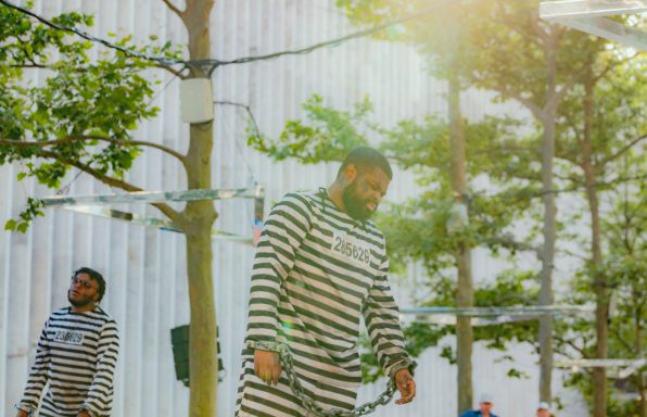 Two men in striped prison uniforms walking outdoors among trees.