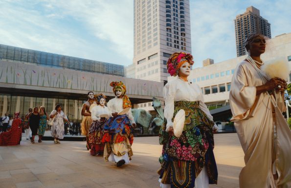 A diverse group of people in colorful traditional costumes parading outdoors.