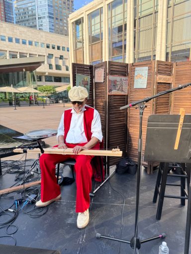 Musician in red and white attire playing an instrument on stage outdoors.