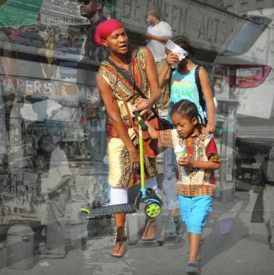 A mother and her children walk together, carrying a scooter amidst a vibrant street scene.