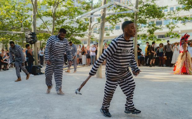 Group of performers in striped prison uniforms moving through an outdoor space.