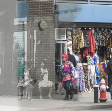 A busy street scene with colorful clothing displayed and a woman walking by.