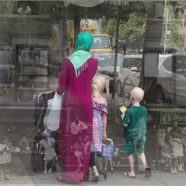 Mother in a green headscarf with her 
 three children, one in a printed dress, walking on a city street with a blurred background.