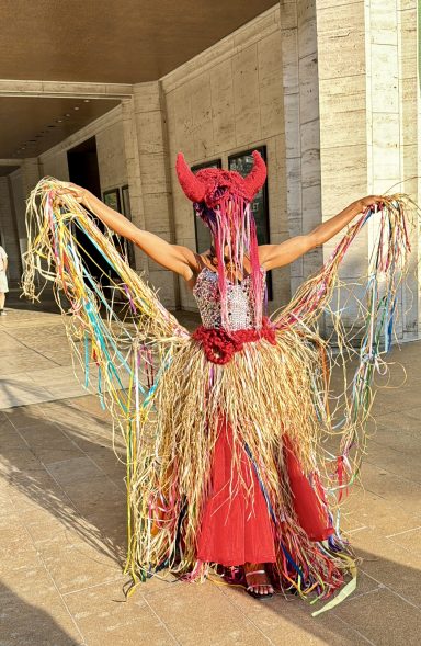 Person wearing a colorful, elaborate costume with horns and flowing, shiny materials.